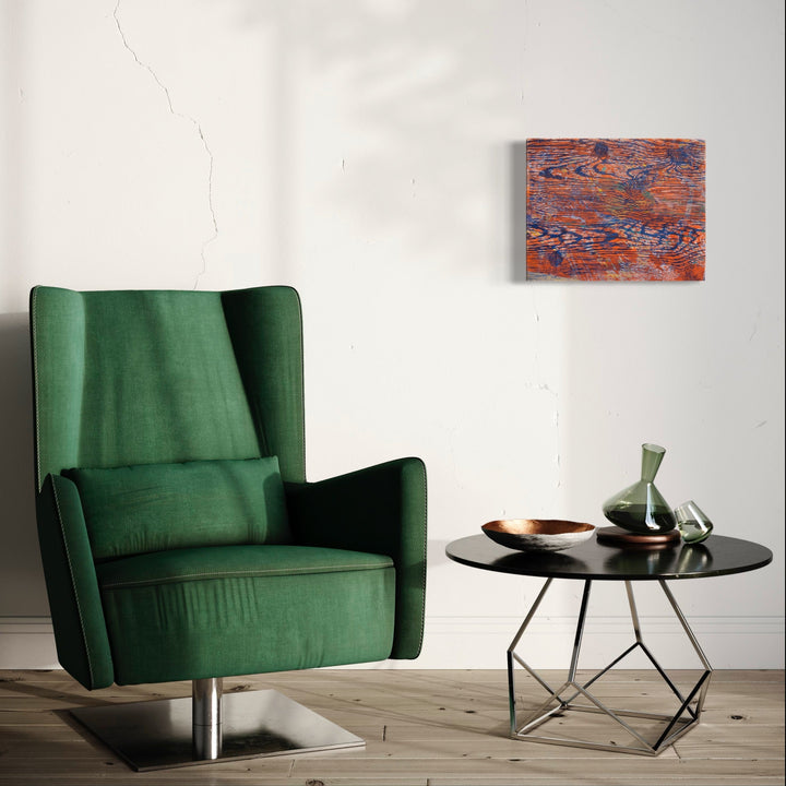 The artwork 'Gutturals' by Emna Zghal features abstract layers of rustic orange and deep blue, creating a weathered, textural effect through woodcut printing and pastel on paper mounted on canvas, displayed above an emerald green armchair and modern black side table in a minimalist interior setting.