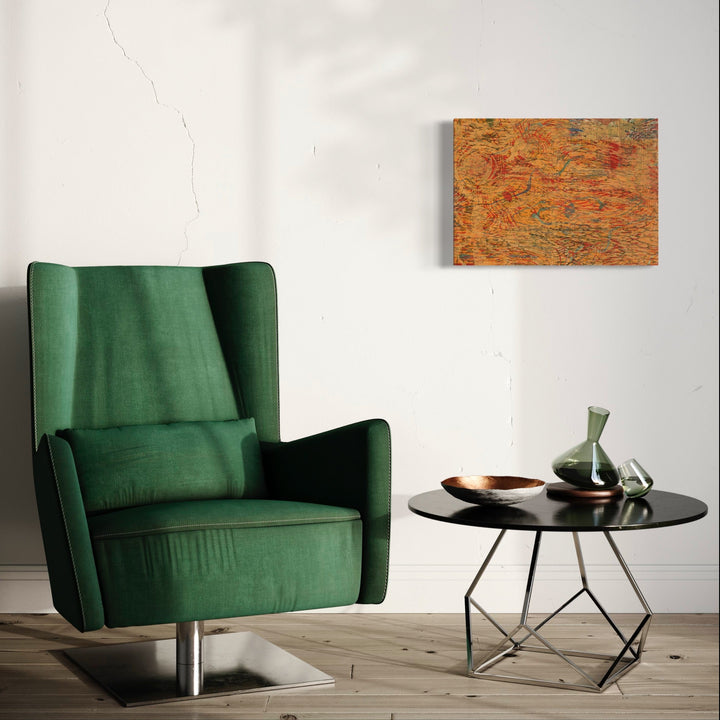 The artwork 'Sun Sliding' by Emna Zghal features abstract woodcut patterns in warm orange and rusty tones mounted on canvas, displayed above a modern emerald green velvet armchair and round black side table in a minimalist interior setting. The woodcut print showcases organic, flowing lines and textural elements. By Emna Zghal.