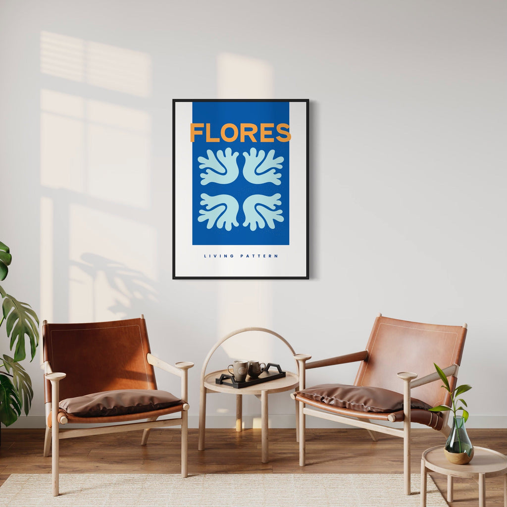 The artwork 'Flores Poster' by Alina Glotova features a minimalist composition with stylized white dove-like shapes arranged in a symmetrical pattern against a vibrant royal blue background. The modern geometric design creates a harmonious four-part motif, framed in black, displayed in a contemporary living space between two leather chairs. 30x40 inches print.