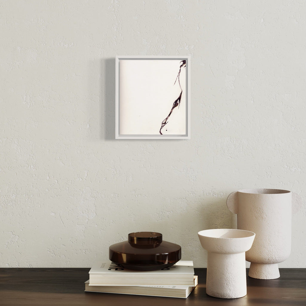The artwork 'Tensile' by Susan Rowe Harrison features a minimalist black ink brushstroke on white paper, creating a dynamic diagonal line that suggests movement and tension. The stark contrast and fluid gesture are elegantly framed in a simple white frame, measuring 9.5 x 10.75 inches.