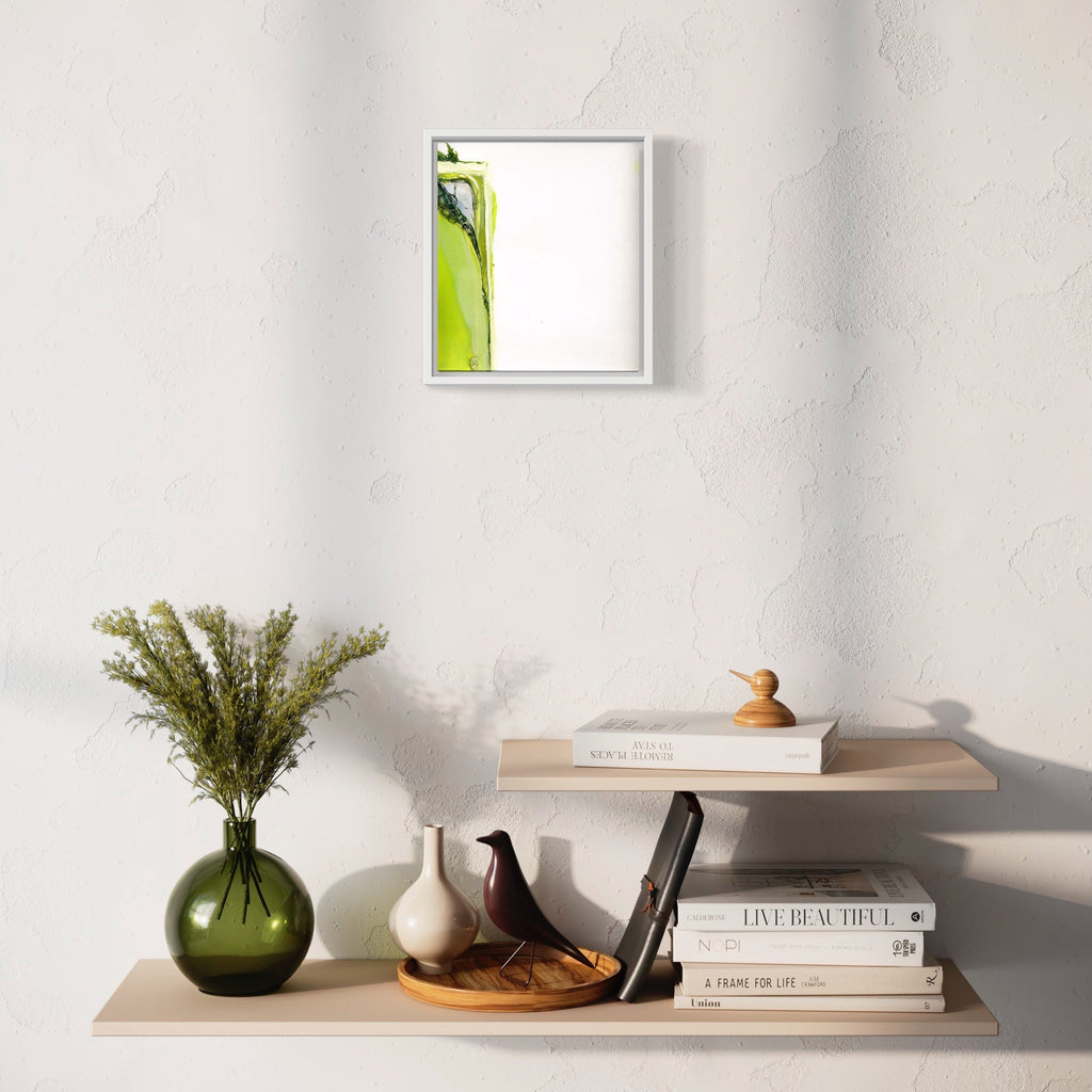 The artwork 'Don't panic 401' by Susan Rowe Harrison features a minimalist framed piece with vibrant lime green abstract forms against white background, displayed above a contemporary styled shelf arrangement with decorative objects, including a green glass vase with dried botanicals, ceramic birds, and stacked books. Art piece by Susan Rowe Harrison.
