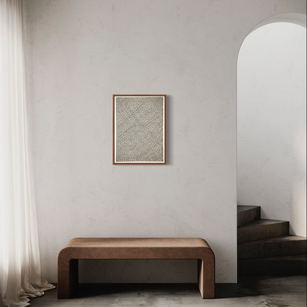 The artwork 'Meditation XXII (open heart)' by Lynnette Therese Sauer features delicate ink patterns on paper, creating an intricate textural composition in soft gray tones. The framed piece showcases a meditative abstract design against a neutral background, displayed above a curved wooden bench in a minimalist interior setting with arched doorway and natural light.
