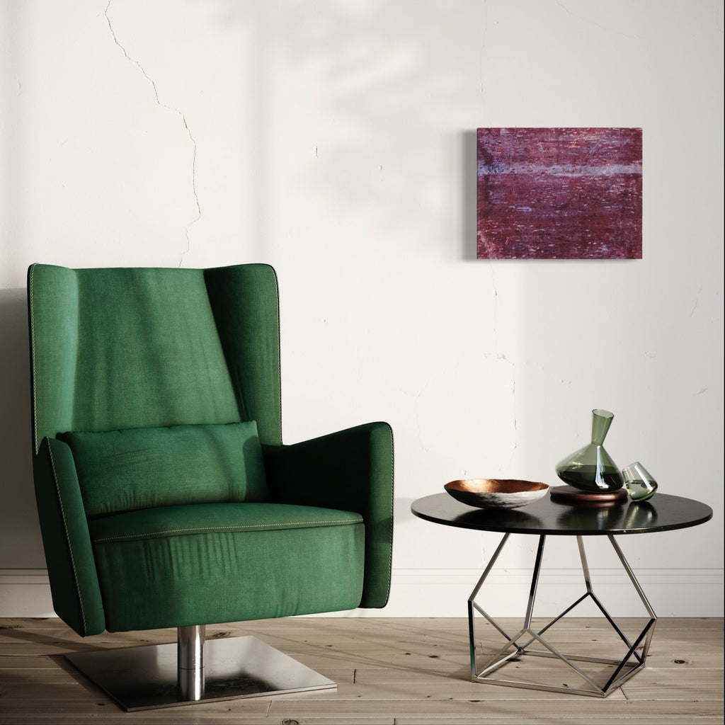 The artwork 'Purple Horizon' by Emna Zghal features abstract layers of deep purple and burgundy hues creating a textured landscape effect. The woodcut print on paper, mounted on canvas, displays rich, organic patterns and subtle variations in color, reminiscent of a distant horizon at dusk. The artistic technique creates a compelling interplay of light and shadow through the wood grain texture.