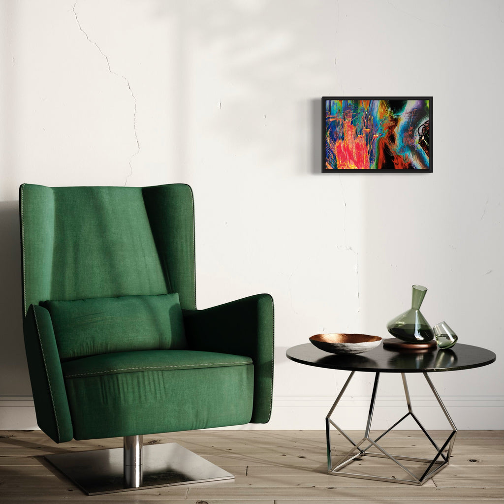 The artwork 'Particle Physics 07' by Chunbum Park features vibrant abstract swirls of red, blue, and turquoise colors in a dynamic composition, displayed in a black frame against a white wall, showcasing alongside a modern emerald green armchair and circular side table, creating a contemporary art setting. Giclee print by Chunbum Park.