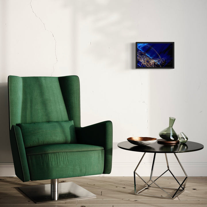 The artwork 'Particle Physics 30' by Chunbum Park features abstract luminous blue streaks against a deep navy background, capturing the dynamic movement of subatomic particles. The framed giclee print showcases swirling golden light trails intertwined with electric blue patterns, creating a mesmerizing visualization of quantum physics in artistic form. Displayed on a white wall above modern furniture.