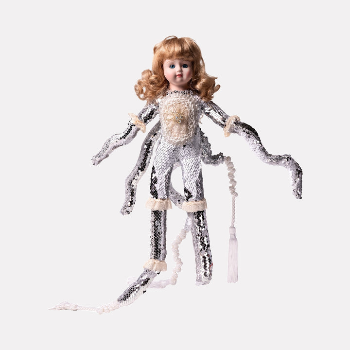 A surreal doll figure with porcelain face and curly hair, dressed in a textured costume with shimmering sequins and soft fabric details, featuring multiple elongated limbs. This unique creation is part of Lisyanet Rodriguez’s "A Worm, a Bird, an Insect, a Human Being…" art collection for Curina.