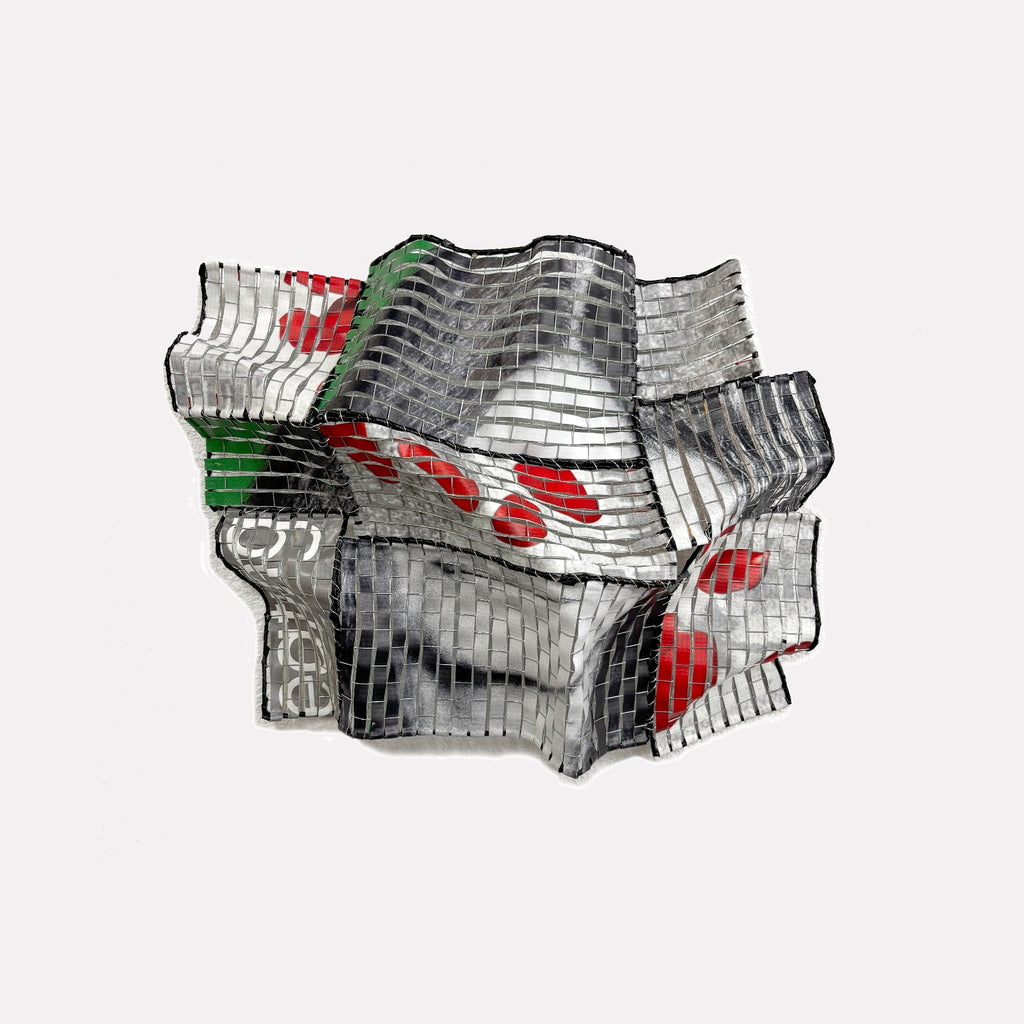 Blind Date by Shelley Heffler is a Curina art piece featuring a distorted metallic mosaic with flowing, ribbon-like shapes in silver, red, green, and black tones, creating an abstract, dynamic form that evokes movement and contemporary industrial elegance.