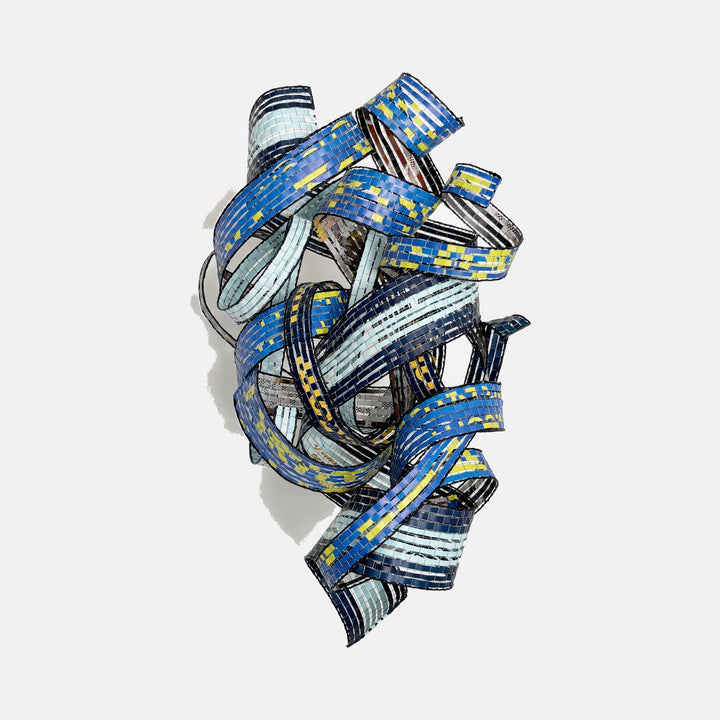 Currents of Change by Shelley Heffler is a Curina art piece showcasing a complex, ribbon-like metallic sculpture in shades of blue and yellow, featuring interwoven bands that create a dynamic, textured form evoking movement and contemporary abstraction.