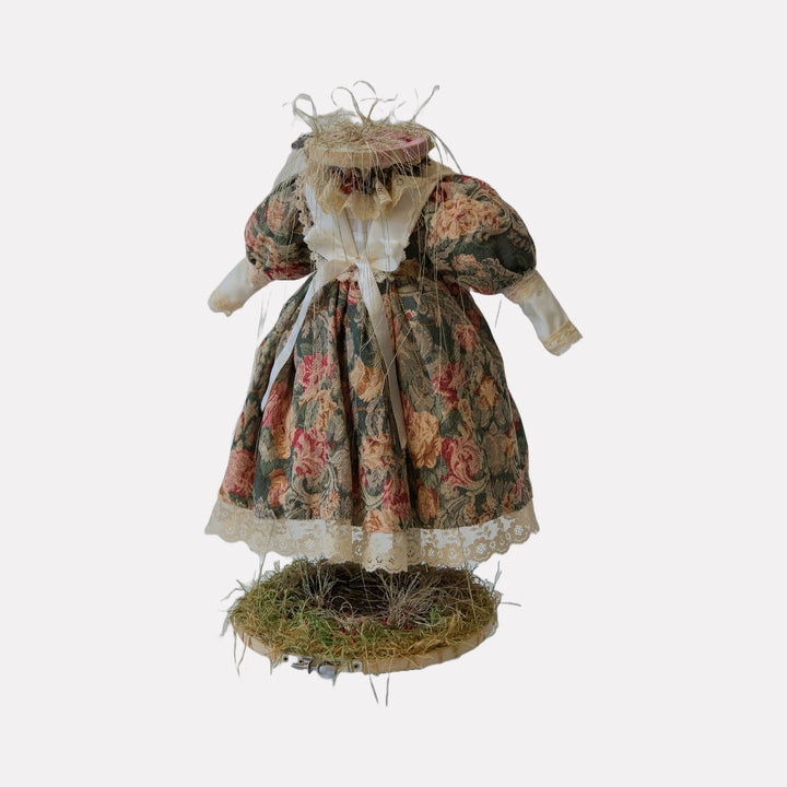 The Red Bird’s Secret Garden by Lisyanet Rodriguez features a whimsical handcrafted dress with voluminous sleeves and floral tapestry fabric, accented with lace and raffia, resting delicately on a natural moss-covered base, evoking a charming, rustic art piece by Curina.
