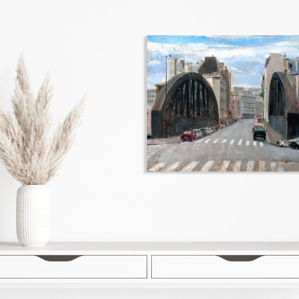 The artwork 'Rue Aqueduc' by Peter Colquhoun depicts an urban street scene with two dramatic arched bridges spanning across the road. Oil on linen captures the soft blue sky, industrial architecture, and city buildings in muted tones. Parked cars line the street, with distinctive crosswalk stripes in the foreground, creating a realistic Montreal cityscape.