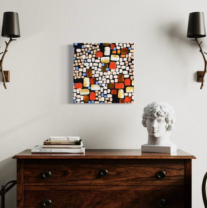 The artwork 'Dark Moon (Le Cape)' by Taylor Binda features a vibrant mosaic-style composition of geometric squares and rectangles in orange, brown, yellow, and white against a black background. The 18x18 inch acrylic painting creates a dynamic pattern reminiscent of stained glass, displaying an abstract modernist style with crisp edges and balanced color distribution.