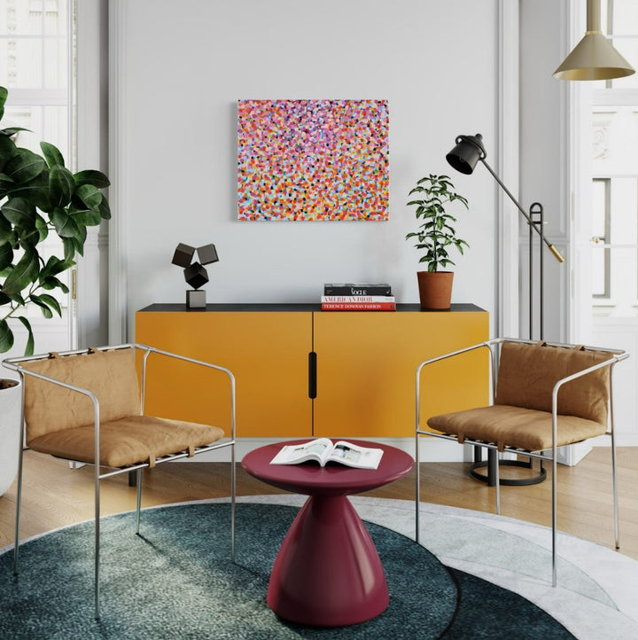 The artwork 'hundreds + thousands' by Taylor Binda features a vibrant pointillist composition of multicolored dots scattered across the canvas. Pink, red, orange, and purple specks create a dynamic confetti-like pattern, suggesting movement and celebration. The acrylic painting on canvas measures 24x30 inches, displaying a contemporary abstract approach that evokes sprinkles or scattered petals in a joyful arrangement.