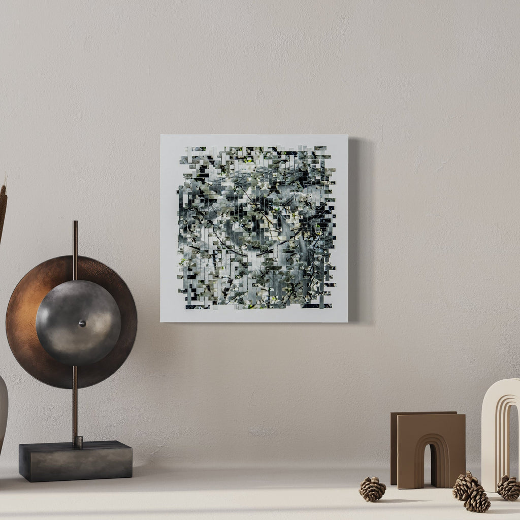 The artwork 'Bloom' by Kiana Honarmand features an intricate mosaic pattern created from hand-cut and woven giclee prints. Abstract black, white, and gray geometric shapes form a complex pixelated composition with subtle yellow accents. The 16x16 inch piece is presented in a minimalist white frame, creating a contemporary digital-meets-traditional aesthetic.