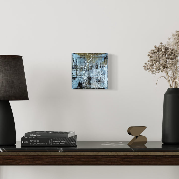The artwork 'Rapture 4' by Bill Burns features a striking abstract composition in metallic acrylic on canvas, displaying layers of icy blue and silvery tones with textured brushstrokes creating a weathered, industrial effect. Dark undertones emerge through distressed surfaces, giving depth and complexity to this 8x8 inch contemporary piece.