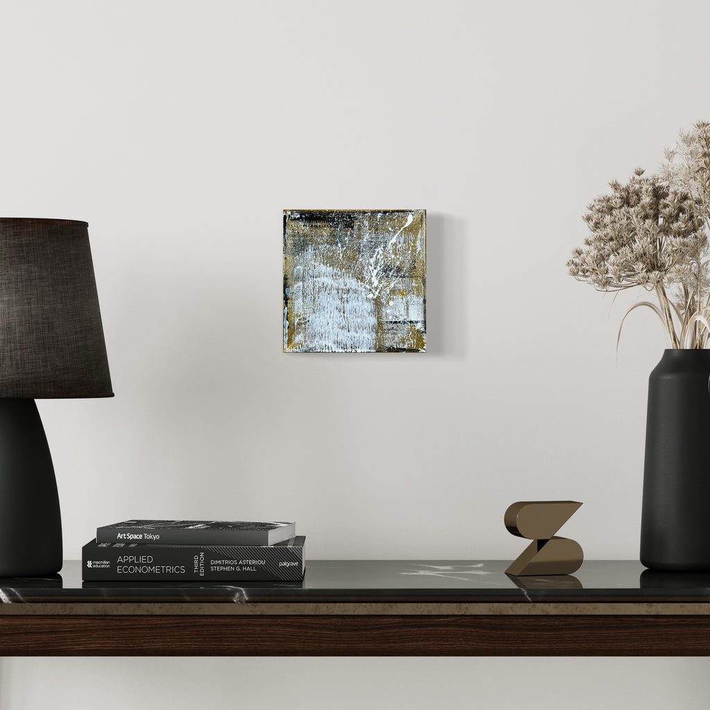 The artwork 'Rapture 5' by Bill Burns features abstract metallic acrylic textures on an 8x8 canvas, displaying a blend of ethereal blue and gold tones with weathered, textural elements creating a dimensional surface that captures light and shadow in a contemporary style.