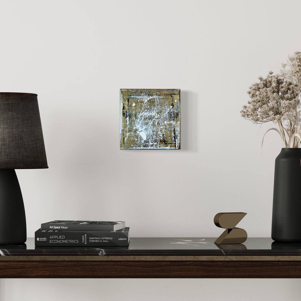 The artwork 'Rapture 6' by Bill Burns features a striking abstract composition in metallic acrylic on canvas, showcasing a weathered, textural surface with shimmering gold and silver tones layered over distressed blues. The 8x8 inch square piece displays an industrial, modern aesthetic with dynamic scratched patterns and oxidized effects, creating depth and visual intrigue.