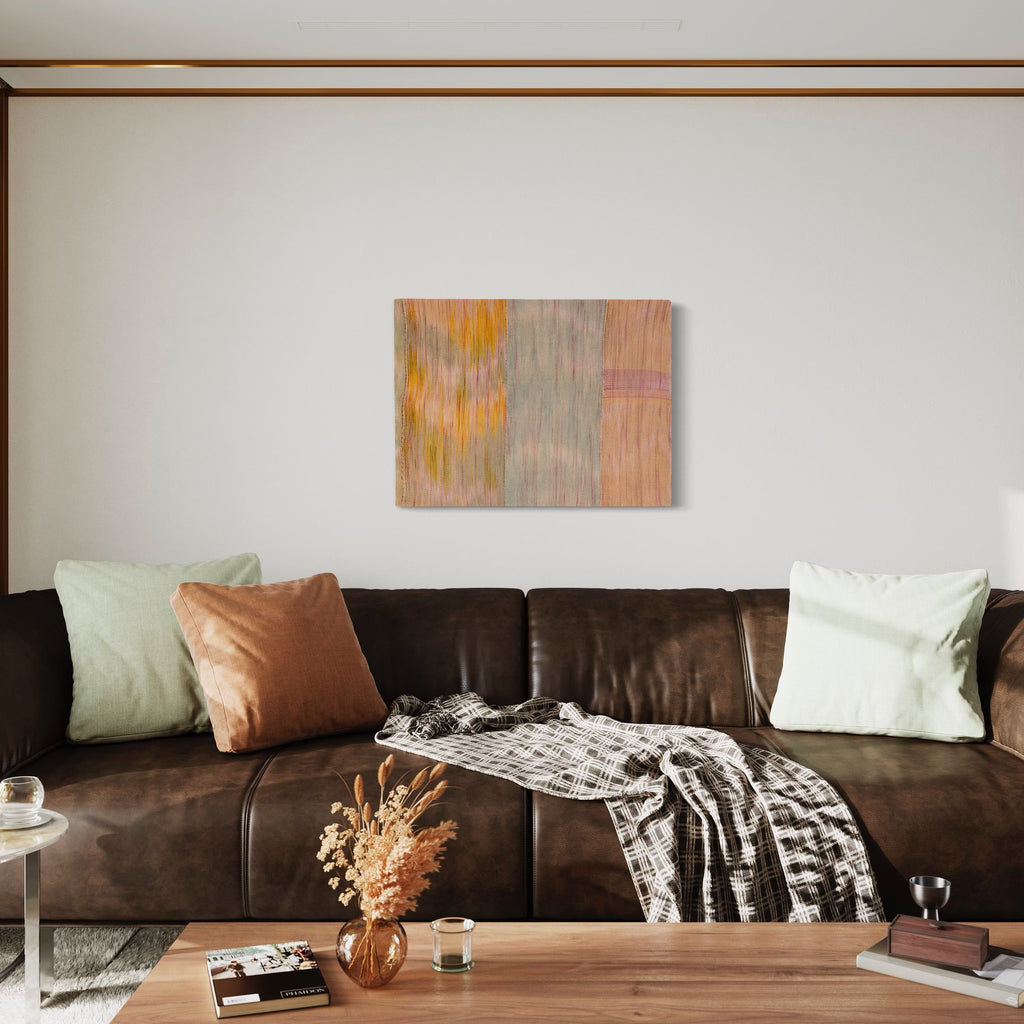 The artwork 'Untitled 107' by Victoria Manganiello features vertical panels of woven fibers in muted peach, sage gray, and golden yellow tones. Abstract brushstroke-like patterns create a gentle vertical movement across the textile surface, with subtle color transitions and textural elements achieved through natural and synthetic fiber blending. 24x32 inches.