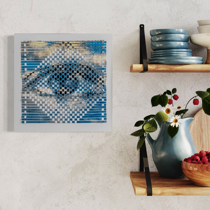 The artwork 'Up or Down' depicts an intricately woven pattern forming an eye using hand-cut digital prints in shades of blue and white. The checkered weaving technique creates a mesmerizing optical illusion, with gradient tones transitioning from deep azure to pale gray across a 16x16 inch square canvas by Kiana Honarmand.