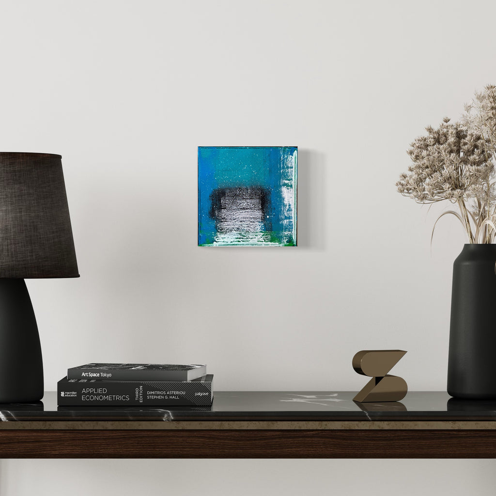 The artwork 'Voyage 2' by Bill Burns features a small square canvas with vibrant turquoise blue borders framing a textured grayscale center. The abstract composition creates a portal-like effect through layered acrylic paint, with rough brushstrokes and distressed textures merging modern and industrial aesthetics in an 8x8 inch format. Artwork by Bill Burns.