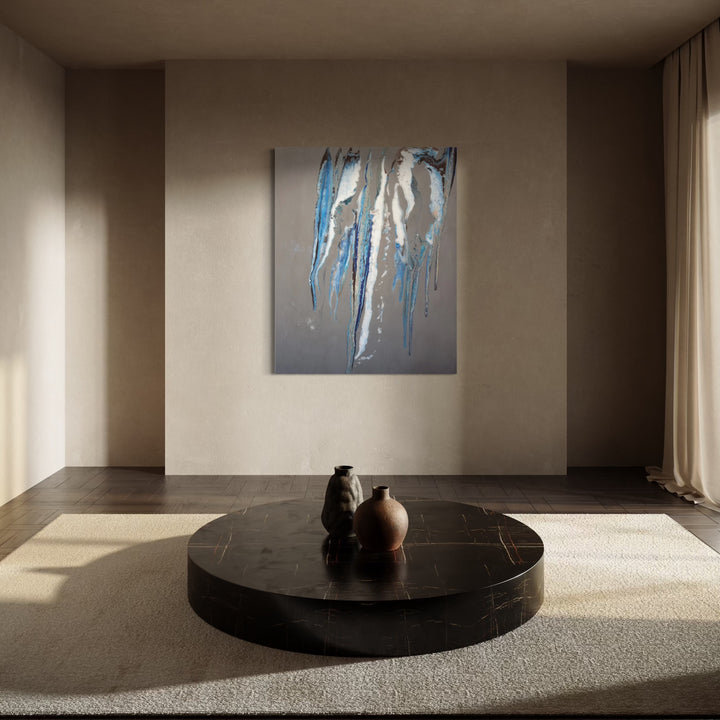 The Wind of Blue by Swann Freslon features dynamic vertical streaks of vibrant blue and soft grays contrasted with white and muted beige, creating an abstract composition that evokes flowing movement and a serene, spacious atmosphere within a calm, minimalist room setting.