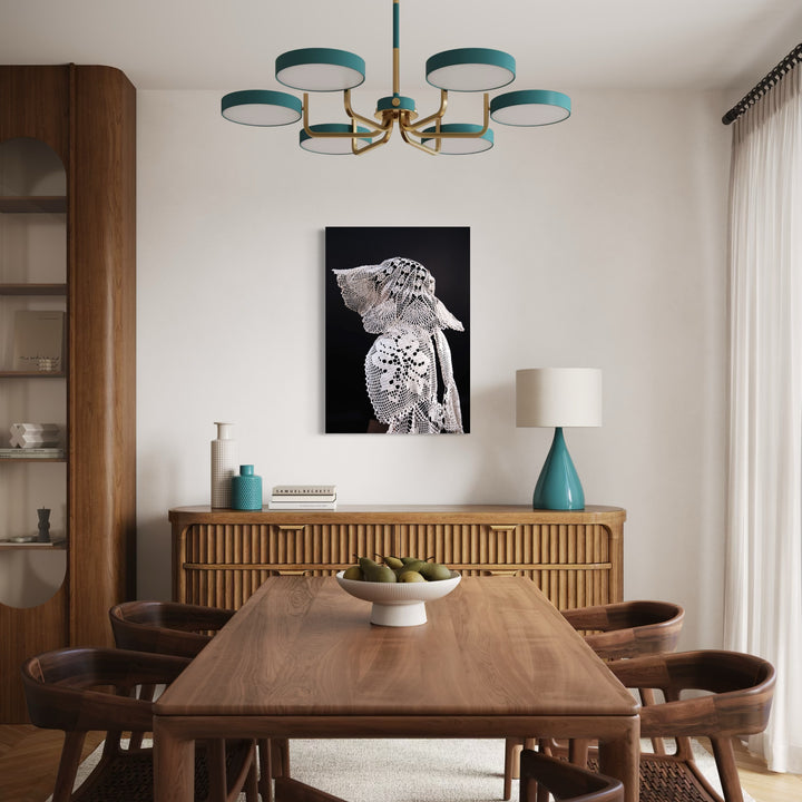 080A8525 by Eunice Pais captures a figure adorned in intricate, lace-like textures with a distinctive headpiece against a deep black backdrop. Positioned above a warm, wooden sideboard in a softly lit dining area, the artwork introduces a refined, serene mood that complements the mid-century modern furnishings and muted color palette.