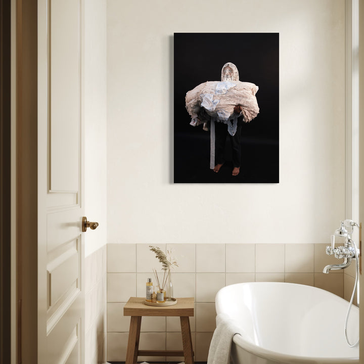 080A8575 by Eunice Pais depicts a figure enveloped in voluminous, textured fabric against a deep black backdrop, evoking a sense of ethereal mystery. Displayed in a softly lit bathroom with neutral tones, the artwork introduces a contemplative and serene presence that complements the minimalist, elegant décor.