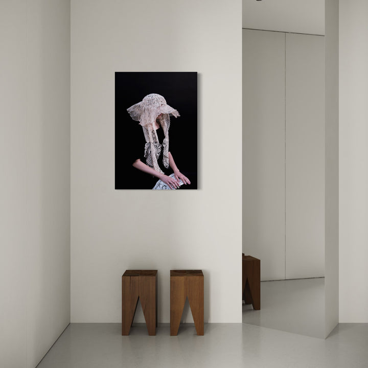 080A86891 by Eunice Pais features a delicate portrait of a figure wearing an intricate lace hat against a deep black background, capturing a sense of elegance and subtle mystery. Displayed in a minimalist room with neutral tones, two wooden stools beneath it add warmth and balance to the serene, refined space.