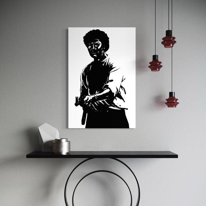 AK47 by Harold Herb features a stark black-and-white silhouette of a man with an afro holding a firearm, presented on a crisp white canvas. Positioned against a minimalist gray wall above a sleek black console with modern geometric decor and deep red pendant lights, the artwork commands a bold, dramatic presence in the contemporary space.