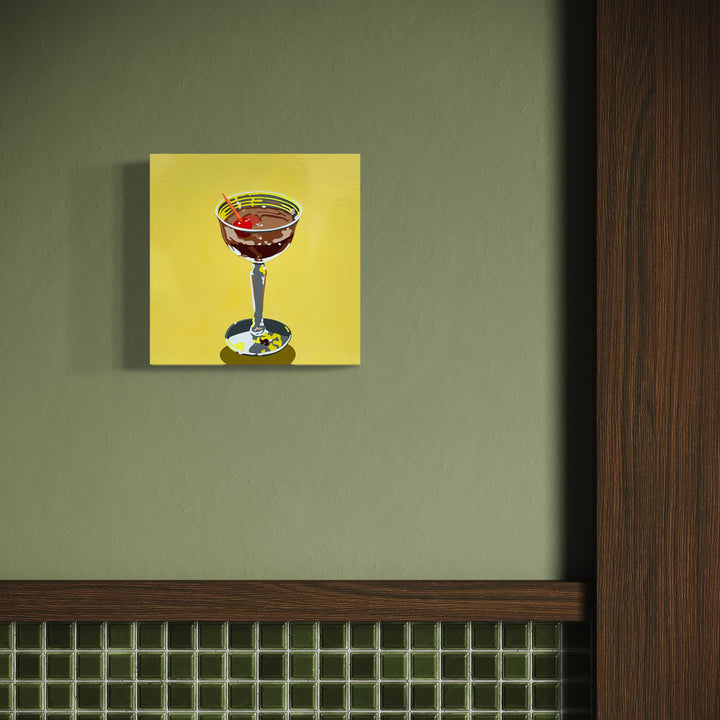 The artwork 'Bourbon Cocktail (on yellow)' by Lori Larusso features a stylized cocktail glass against a vibrant yellow background. The glass contains a rich amber-red bourbon with a cherry garnish, painted in a clean, graphic style using acrylic and enamel on wood panel. The composition shows precise linework and bold color blocking, creating a modern pop art aesthetic.