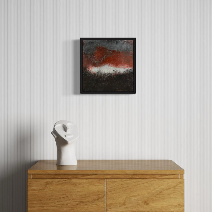 The artwork 'Closing: The Season Ends' by Karen L. Burns features a dramatic abstract landscape with a bold rust-red horizon against a textured black foreground and misty white center. The acrylic painting showcases a moody, atmospheric effect through layered mixed media techniques, displayed in a sleek black frame against a white wall. - Karen L. Burns
