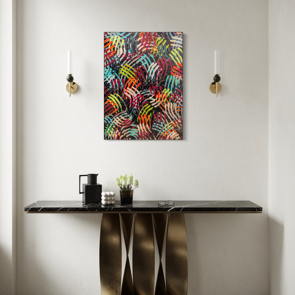 Cosmic Dance by Hillary Hany features a vibrant, abstract composition of overlapping, multicolored curved lines creating a dynamic, rhythmic pattern. Displayed against a neutral wall over a sleek black marble console table with sculptural brass legs, flanked by minimalist wall sconces, it brings energetic movement and modern elegance to the space.