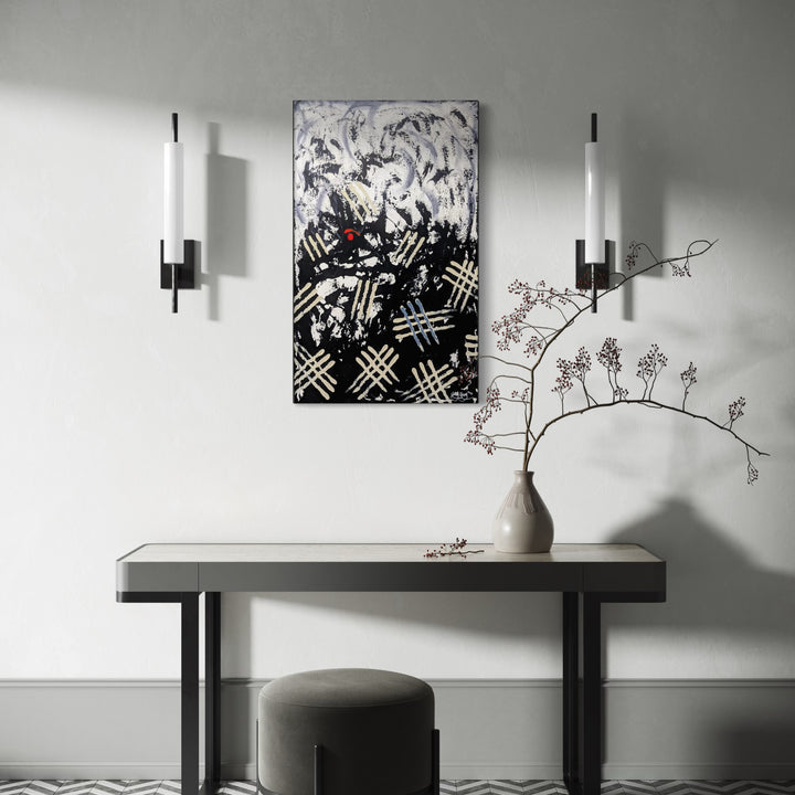 Darkness Within by Hillary Hany presents a stark abstract composition with bold black and white contrasts, featuring textured, chaotic marks and a striking red accent. Mounted above a minimalist console table beside delicate wall sconces and a sculptural vase with fine branches, it imbues the space with a moody, contemplative energy.