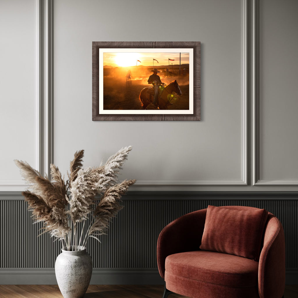 Echoes of the Frontier by Kyle Murphy captures a golden sunset scene with a cowboy on horseback emerging through dust in a rodeo arena, illuminated by warm light and framed by waving flags, evoking the rugged spirit and timeless energy of the Western frontier.