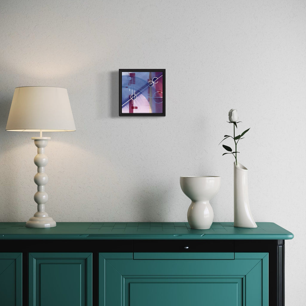 The artwork 'Exoplanet' by Arthur Norcome features abstract watercolor composition in vibrant purple and pink hues with geometric intersecting lines, displayed in a black frame. 8x8 inch painting showcases modernist style, mounted on white wall above teal cabinet, complementing minimalist home decor setting by Arthur Norcome.