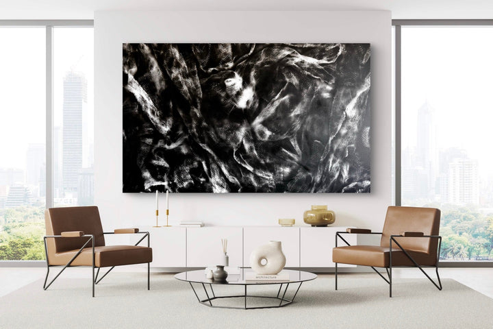 The artwork 'Fantome' by Gina Iannucci features dramatic black and white abstract patterns created with spray paint on canvas. Swirling, smoke-like textures create a dynamic ethereal movement across the large-scale composition. Bold contrasts between light and dark elements evoke a mysterious, ghostly atmosphere, displayed in a modern minimalist living space. Size: 58x96 inches.