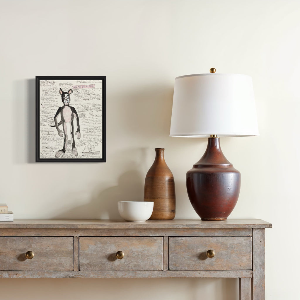 How To Be A Dog by Jody MacDonald: Whimsical ink sketch of bunny figure in black frame, displayed above rustic console with ceramic lamps