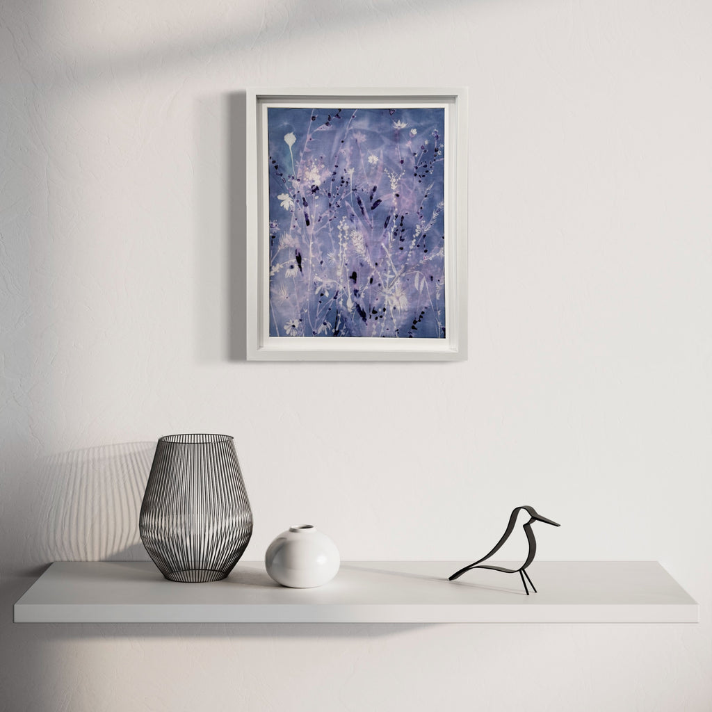 The artwork 'Iced Sky II' by Rachel Kohn features ethereal swirls of periwinkle and lavender hues, with splattered white accents resembling stars or frost crystals against a deep blue background. Created using dye, bleach, and acrylic on cotton, the abstract composition evokes a dreamy winter night sky with its flowing, organic patterns and celestial-inspired elements in a white frame.