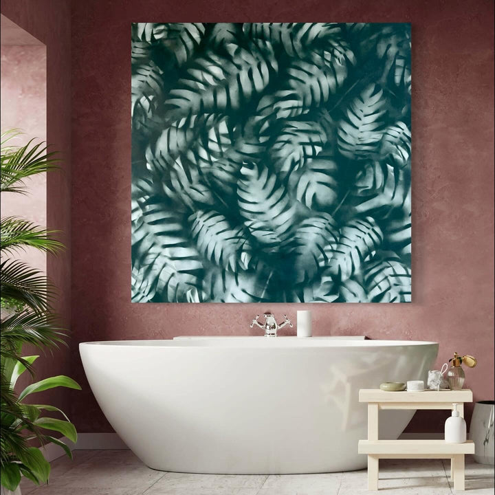 The artwork 'Lush' by Gina Iannucci features ethereal fern patterns in deep teal and white, creating a mesmerizing tropical motif through spray paint techniques on canvas. The overlapping fronds create a dynamic sense of depth and movement, with delicate shadows and highlights dancing across the 58-inch square composition. The misty, dreamlike quality evokes a serene rainforest atmosphere. By Gina Iannucci.