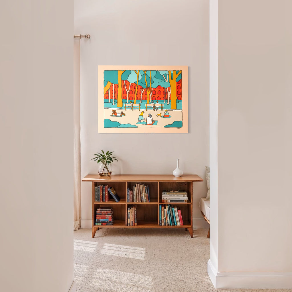 NYC Vibes by Alimo features a colorful scene of people enjoying a sunny urban park framed by tall trees and distinctive red buildings, displayed above a wooden bookshelf in a bright, minimalist room, capturing a playful and lively artistic atmosphere.