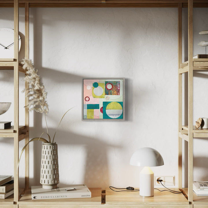 The artwork 'Opposite Attraction' by Giliane Bader features a geometric abstract composition with vibrant circles and rectangles in turquoise, yellow, pink, and green. Created using mixed media on birch panel with cold wax finish, the 12x12 inch piece displays a harmonious balance of shapes against a light background. Artwork by Giliane Bader.