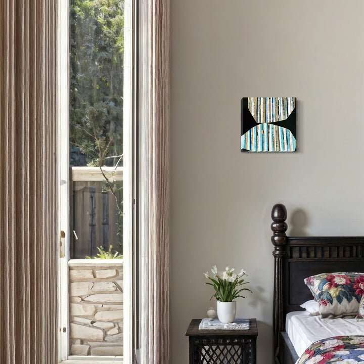 The artwork 'Power of Touch' features vertical turquoise and white striped patterns creating an abstract hourglass shape against a black background. The modern collage artwork mounted on a light gray wall creates a striking visual contrast in a bedroom setting. 12x12 inches mixed media collage by Nicole Hitchcock.