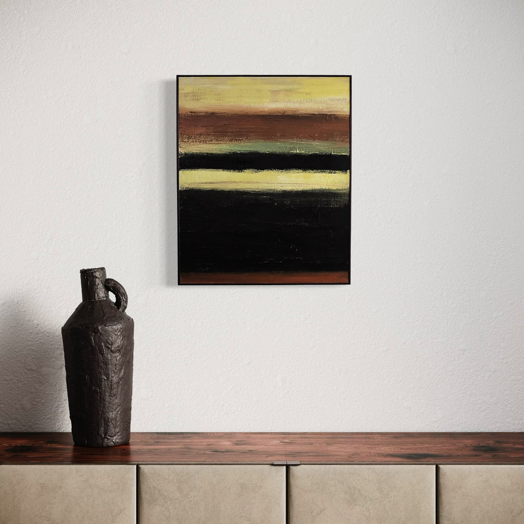 The artwork 'Rustic #2' by Vanessa Ryan features horizontal bands of rich earth tones, with deep black, warm browns, and soft yellow hues creating a minimalist abstract landscape composition. Textured acrylic brushstrokes on canvas suggest a contemplative horizon, measuring 24x20 inches, framed in sleek black.