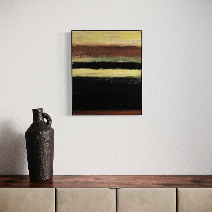 The artwork 'Rustic #2' by Vanessa Ryan features horizontal bands of rich earth tones, with deep black, warm browns, and soft yellow hues creating a minimalist abstract landscape composition. Textured acrylic brushstrokes on canvas suggest a contemplative horizon, measuring 24x20 inches, framed in sleek black.