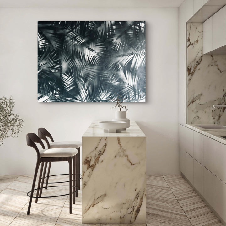The artwork 'Selva' features a mesmerizing monochromatic composition of overlapping palm fronds creating a dynamic pattern in shades of grey and silver. The spray paint on canvas technique gives depth and movement to the tropical foliage design, measuring 36x48 inches. By Gina Iannucci.