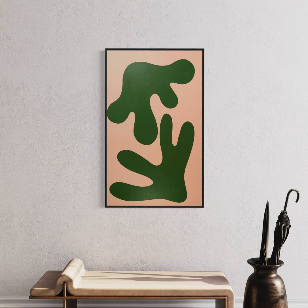 The artwork 'STAGHORN II' by Shadia Sabagh features bold organic shapes in deep forest green against a soft peach background. The minimalist composition depicts abstract, curving forms reminiscent of fern leaves or coral branches, creating a striking modern botanical silhouette within a sleek black frame. Acrylic on canvas, measuring 30x49 inches.