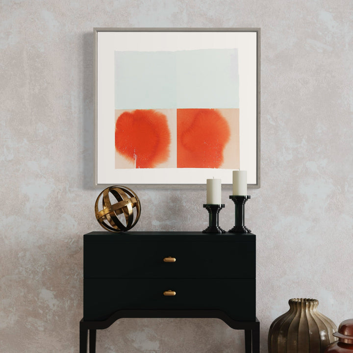 The artwork 'Same/different under a clotted sky' by Ken Schiano features two vibrant coral-orange watercolor forms on white paper, displayed in a minimalist silver frame. Each form appears as a diffused, organic shape with soft edges, creating a striking contrast against the pure white background. The composition evokes a sense of balance and contemplation through its paired abstract forms.