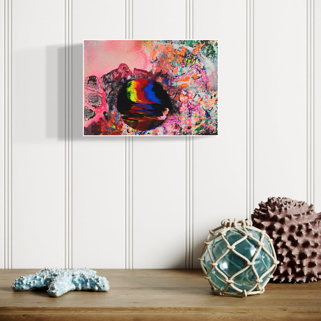 The artwork 'Slippery Planet' by Millie Benson features a vibrant abstract composition with a swirling cosmic sphere in rainbow hues of blue, red, and yellow against a pink atmospheric background. Expressive paint splatters and organic patterns in turquoise and coral create a dynamic, otherworldly effect achieved through mixed media techniques on wood.