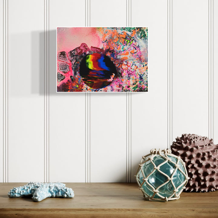 The artwork 'Slippery Planet' by Millie Benson features a vibrant abstract composition with a swirling cosmic sphere in rainbow hues of blue, red, and yellow against a pink atmospheric background. Expressive paint splatters and organic patterns in turquoise and coral create a dynamic, otherworldly effect achieved through mixed media techniques on wood.