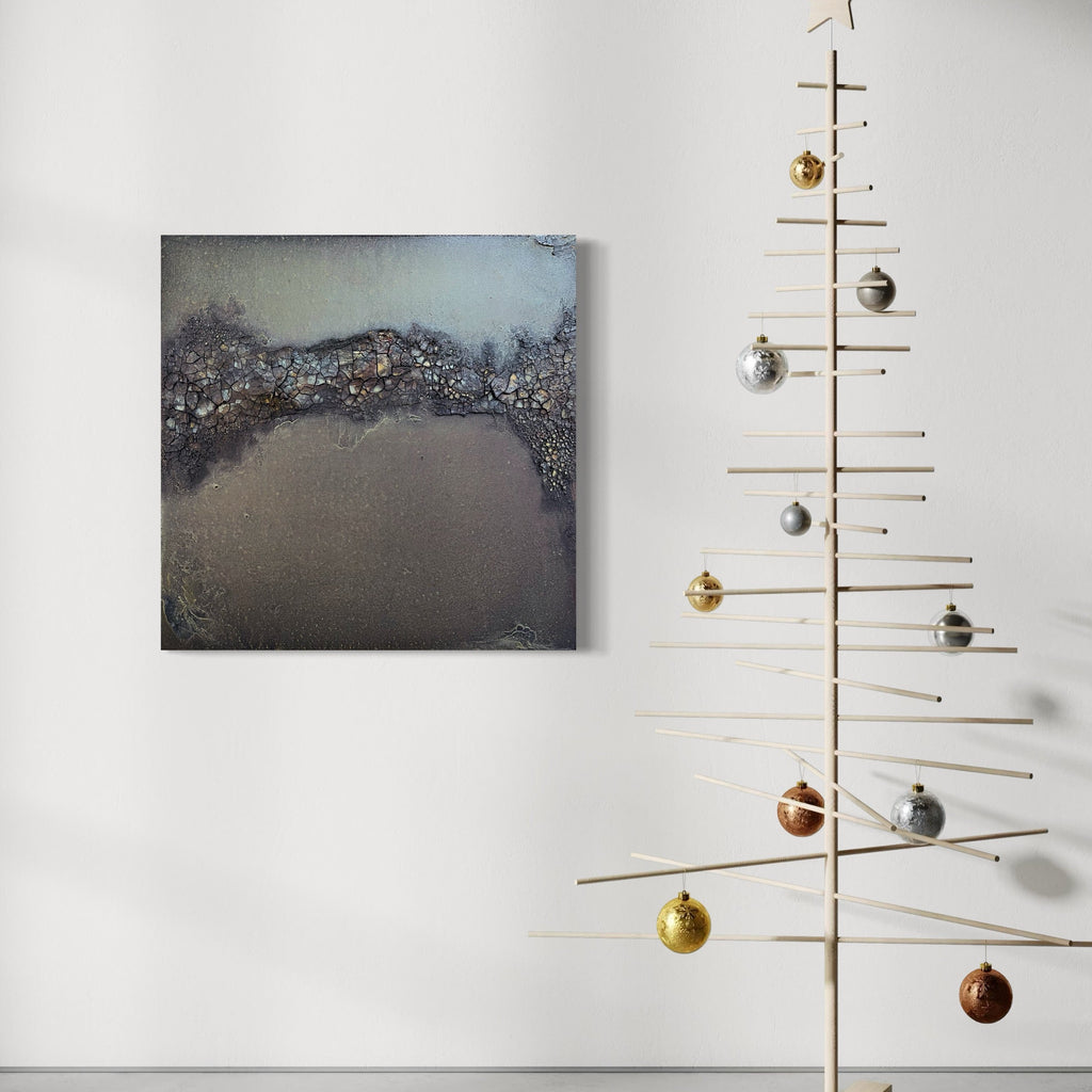 The artwork 'Smoke and Ember' by Abbey Stace features a textured abstract composition with a dramatic interplay of dark charcoal and smoky grays. The surface showcases a rich, granular texture created with plaster and sand, while metallic accents shimmer across the upper portion. The 30x30 inch piece conveys a moody, atmospheric landscape with a distinctive horizon line dividing rough and smooth textures.
