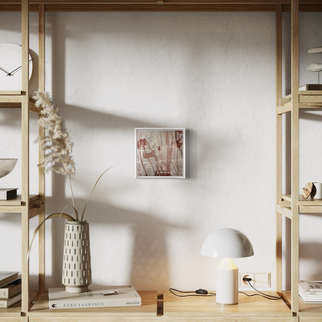 The artwork 'Soma' by Amy Hughes displayed in a minimalist interior setting with wooden shelving, featuring soft pink and red abstract brushstrokes on a 10x10 inch canvas. The oil painting creates a delicate interplay of light and shadow, complemented by surrounding decor including a white dome lamp and dried florals in a textured ceramic vase. By Amy Hughes.